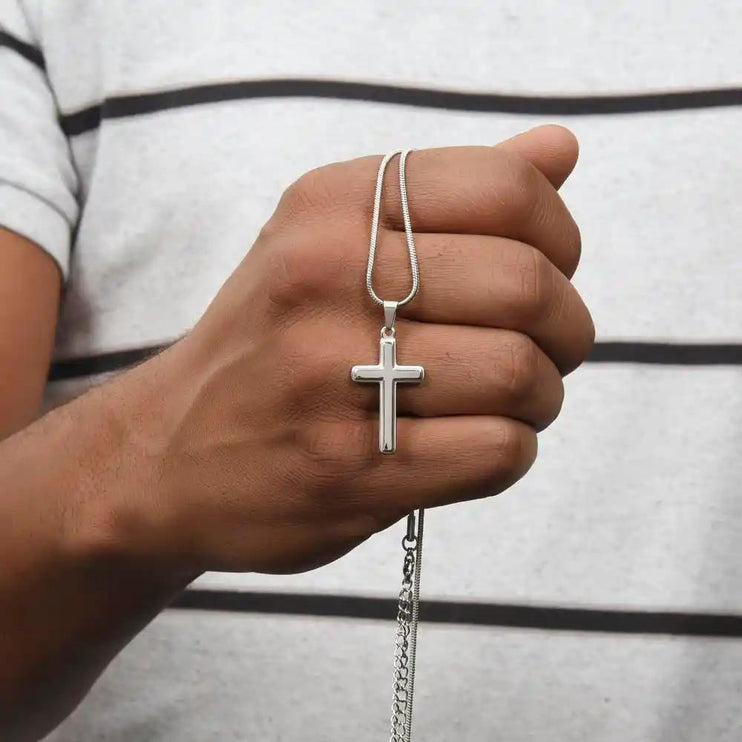 a cross pendant necklace in models hands.