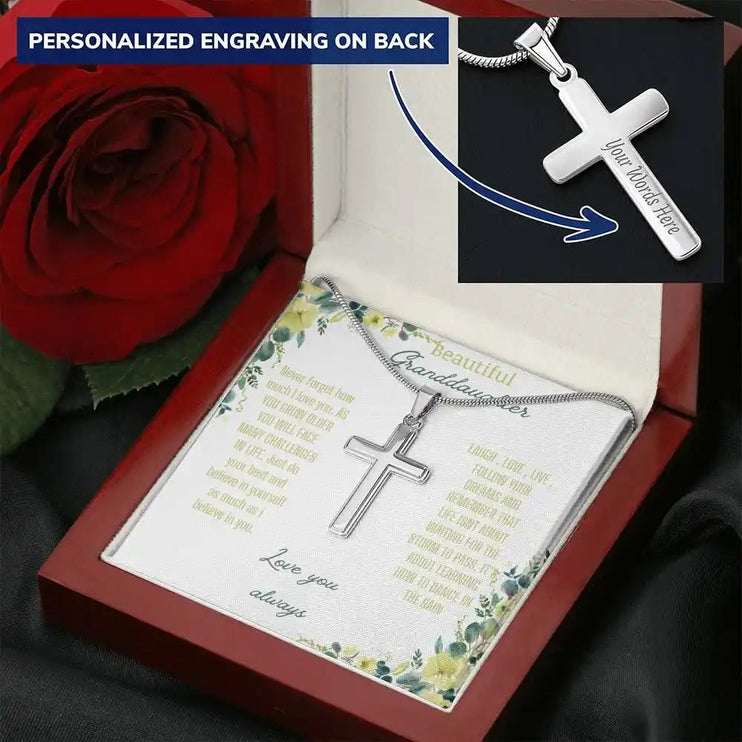 Personalized Cross Necklace with a polished stainless-steel cross and a to granddaughter greeting card in a mahogany box on a black table with a red rose angled slightly left