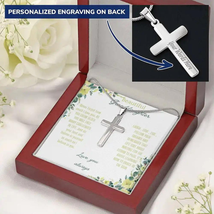 Personalized Cross Necklace with a polished stainless-steel cross and a to granddaughter greeting card in a mahogany box on a white cloth backdrop and white flowers angled slightly left