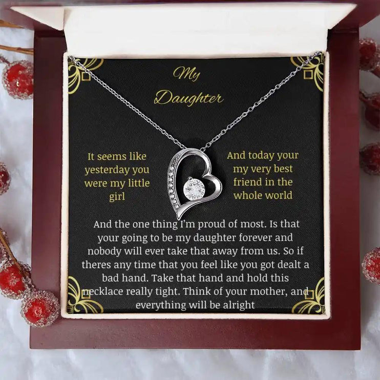 Forever Love Necklace with a white gold charm in a mahogany box with a to daughter from mom greeting card on a white table looking down