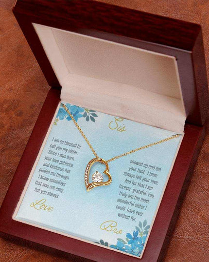 Forever Love Necklace with a yellow gold variant on a to sis from bro greeting card close up view in a mahogany box angled slightly to the right on a rustic brown table.