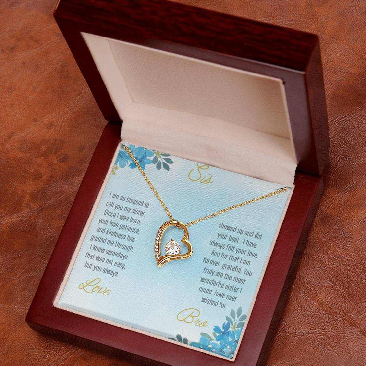 Forever Love Necklace with a yellow gold variant on a to sis from bro greeting card close up view in a mahogany box angled slightly to the right on a rustic brown table.