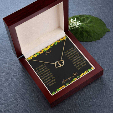 Everlasting Love Necklace with a to sis from sis greeting card inside a mahogany box sitting on a dark grey table with a green leaf beside it further away view