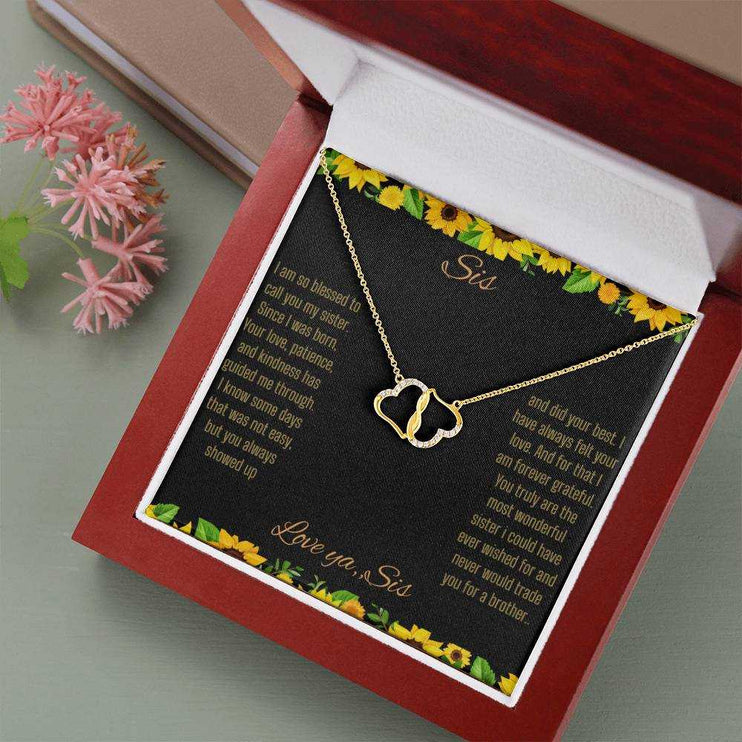 Everlasting Love Necklace with a to sis from sis greeting card inside a mahogany box sitting on a olive colored table with a pink flower beside it angled slightly to the right