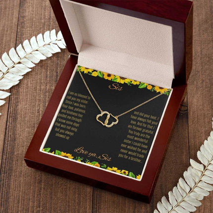 Everlasting Love Necklace with a to sis from sis greeting card inside a mahogany box sitting on a wood grain table with a white fern leaf