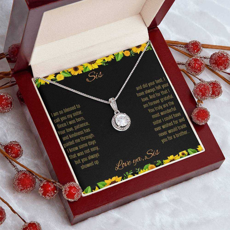 Eternal Hope Necklace on a To Sis from Sis greeting card in a mahogany box angled to the right sitting on a white table cloth with red flower bud stemsclose up view.