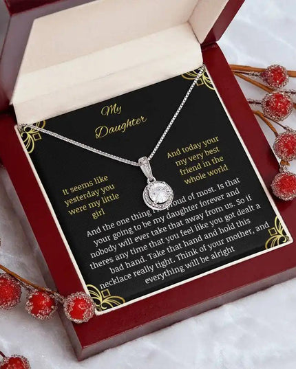 Eternal Hope Necklace in a mahogany box with a to daughter from mom greeting card angled to the right on a white table with red flower beeds