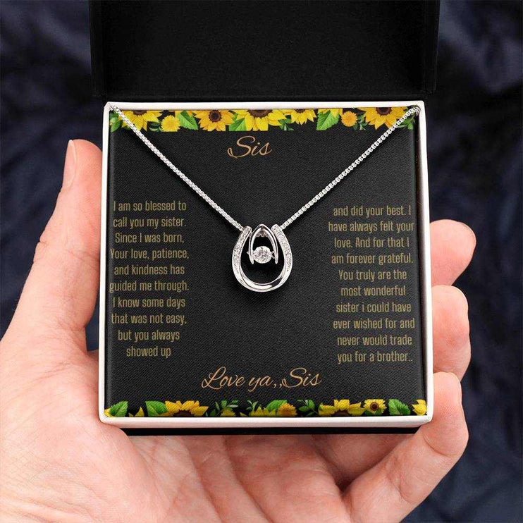 Lucky In Love Necklace with a white gold charm on a To Sis From Sis greeting card in a two-tone box in a models hand