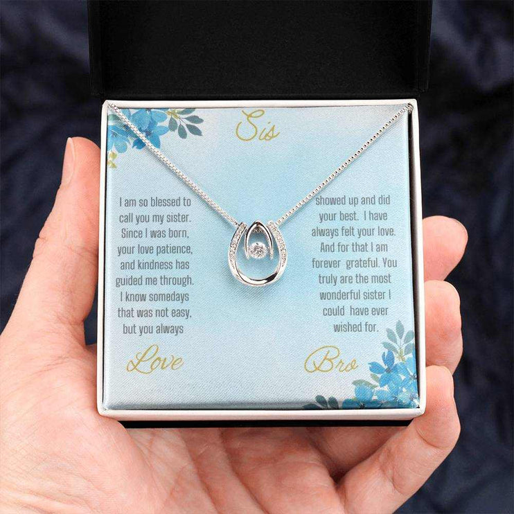 Lucky In Love Necklace with a white gold charm on a To Sis From Bro greeting card in a two-tone box up close in a models hand
