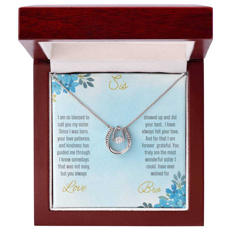 Lucky In Love Necklace with a white gold charm on a To Sis From Bro greeting card up close in a mahogany box