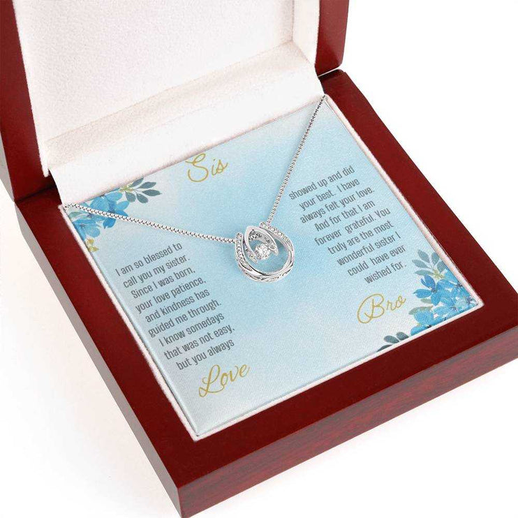 Lucky In Love Necklace with a white gold charm on a To Sis From Bro greeting card up close in a mahogany box angled slightly to the left