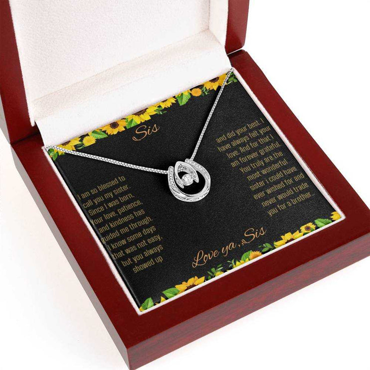 Lucky In Love Necklace with a white gold charm on a To Sis From Sis greeting card up close view in a mahogany box angled slightly to left side