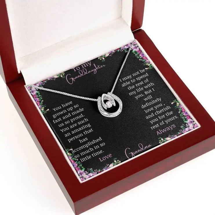 Lucky In Love Necklace with a white gold charm with a to granddaughter from grandma greeting card in a mahogany box on a white background angled to right