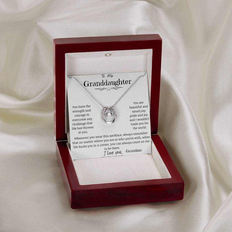 A white gold lucky in love necklace in a mahogany box on a white cloth