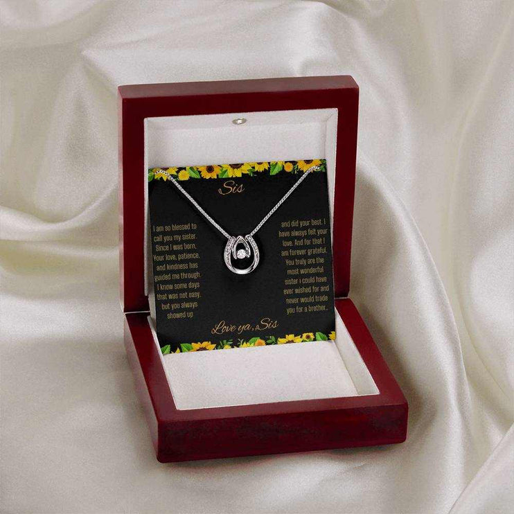 Lucky In Love Necklace with a white gold charm on a To Sis From Sis greeting card up close view in a mahogany box on a drop cloth