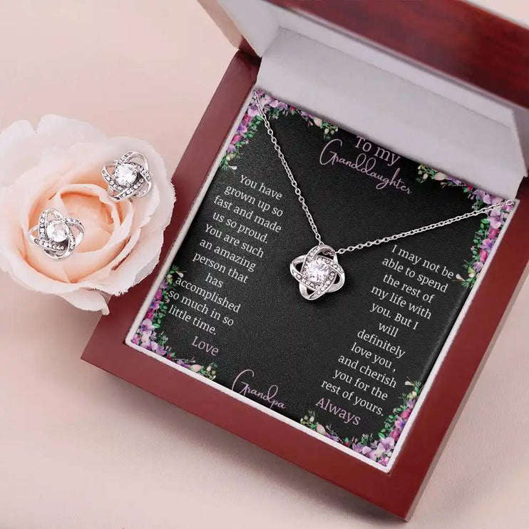 Love Knot Necklace Love Knot Earring Set with a white gold pendant and a to granddaughter from grandma greeting card in a mahogany box angled to the left with earrings on top of a peach rose on the left side of box