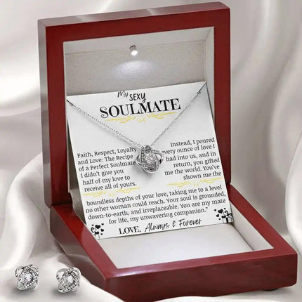 a love knot necklace love knot earring set in a mahogany box on a white cloth.