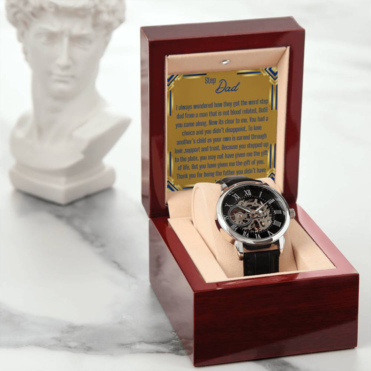 a men's openwork watch in a mahogany box with to stepdad greeting next to a statue.