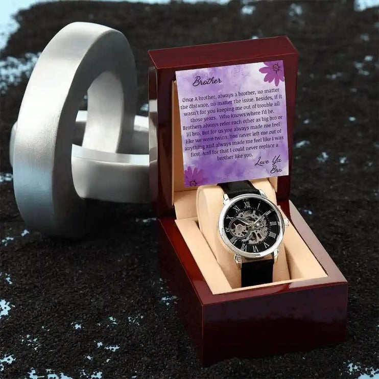 A men's openwork watch and a to brother greeting card in a mahogany box next to design piece.