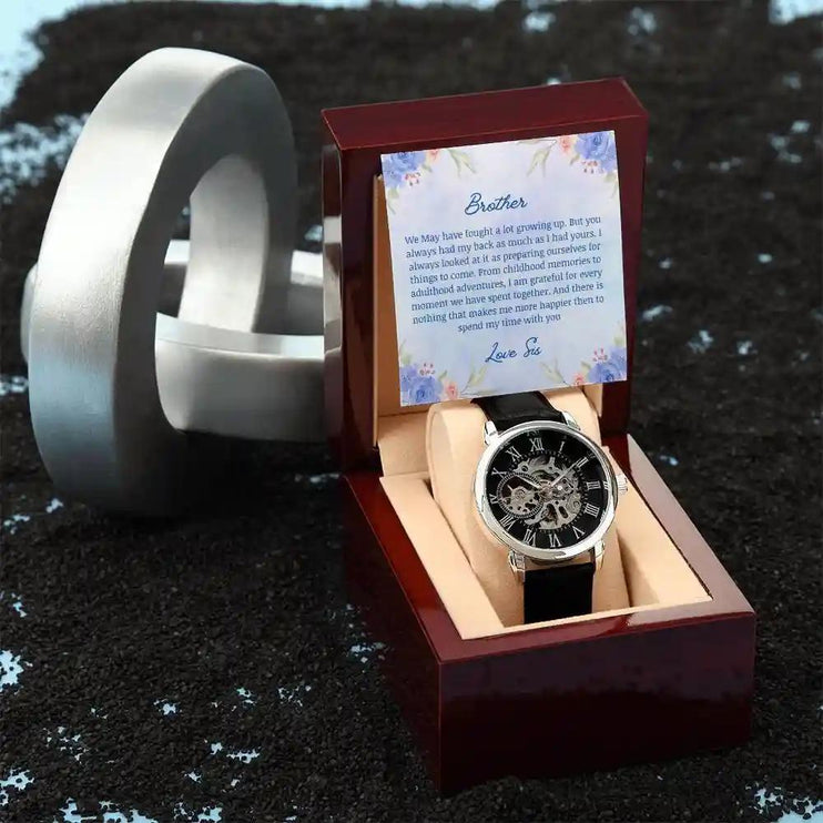 A Men's Open work Watch and to brother greeting card inside a mahogany box on a black table.