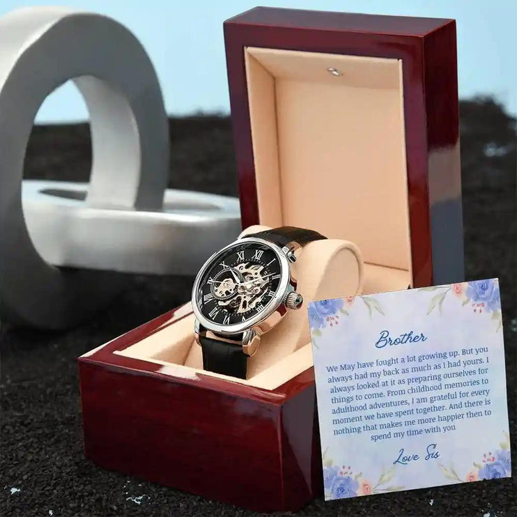 A Men's Open work Watch and to brother greeting card outside of a mahogany box angled to the right.