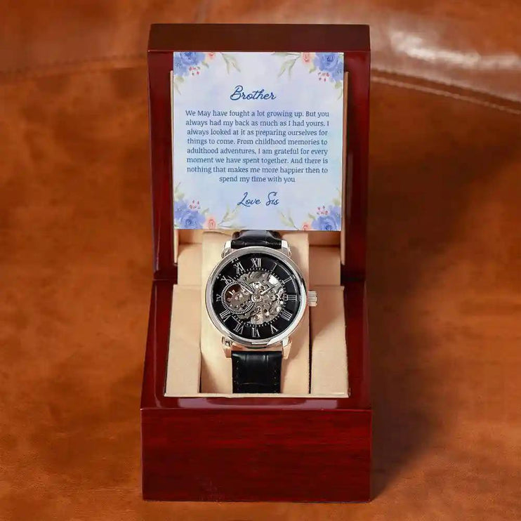 A Men's Open work Watch and to brother greeting card inside a mahogany box on a brown table.