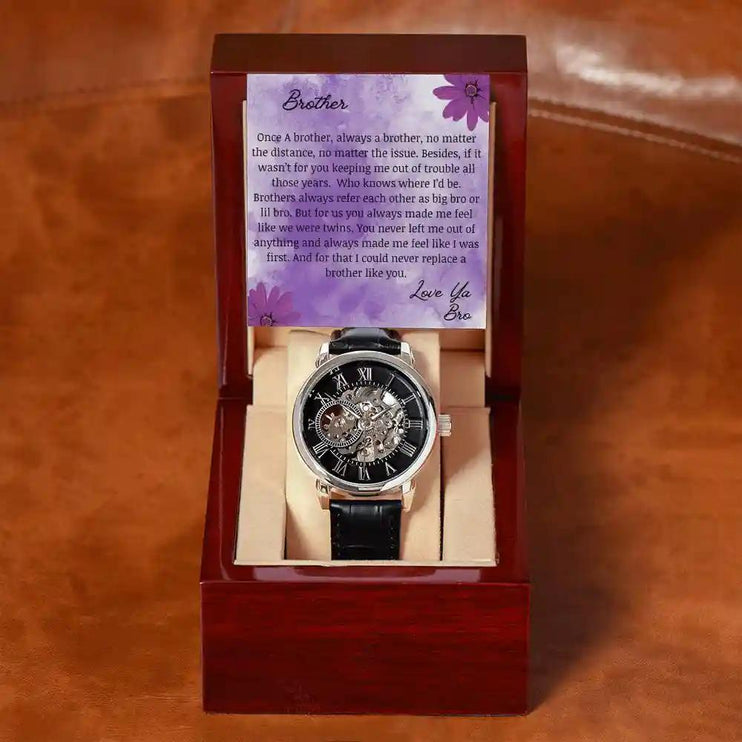A men's openwork watch and a to brother greeting card in a mahogany box on a table.