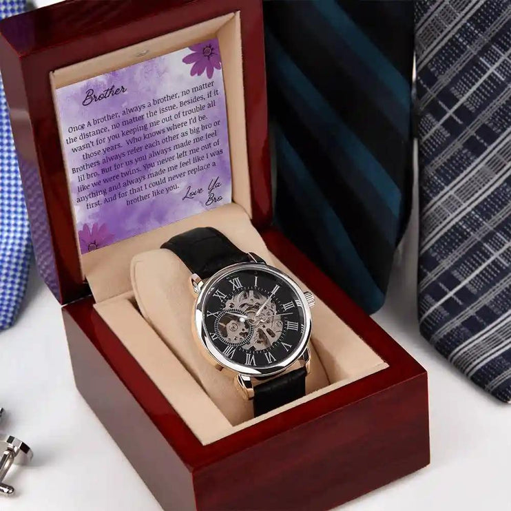A men's openwork watch and a to brother greeting card in a mahogany box on a nightstand.