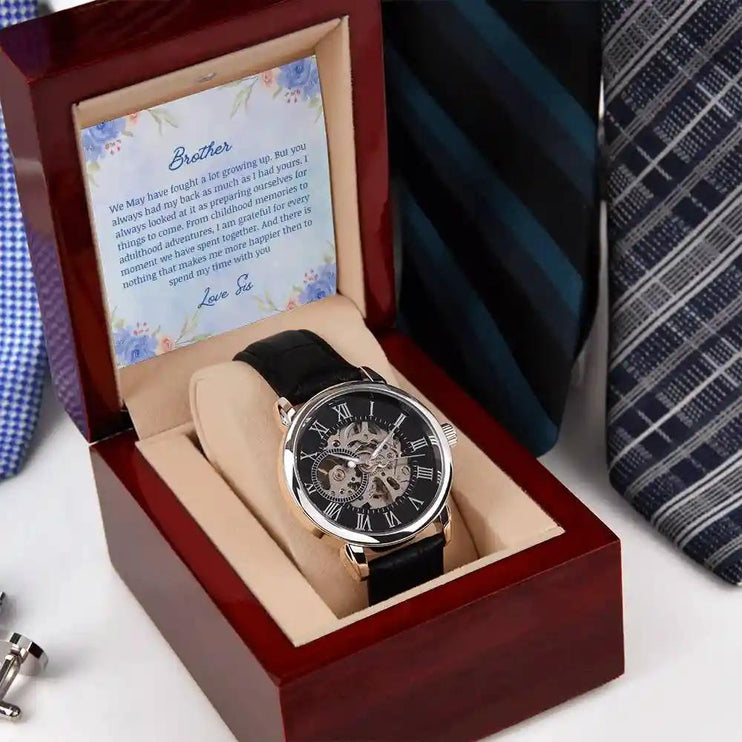 A Men's Open work Watch and to brother greeting card inside a mahogany box on a nightstand.