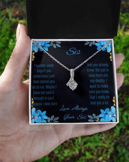 A Alluring Beauty Necklace with a white gold variant on a to sis from sis greeting card inside a two-tone box in a models hand.