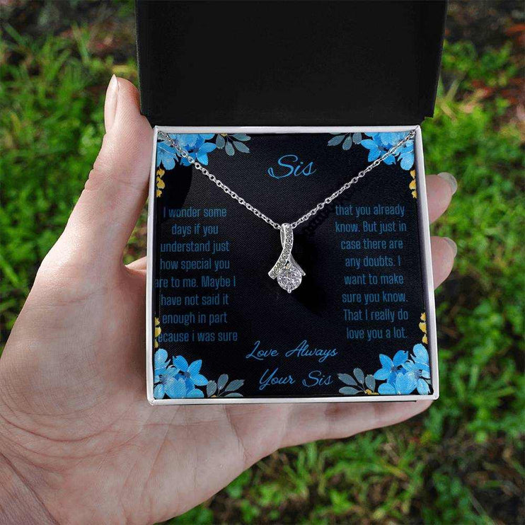 A Alluring Beauty Necklace with a white gold variant on a to sis from sis greeting card inside a two-tone box in a models hand.
