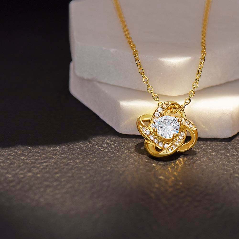 18k gold love knot necklace on a white display