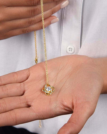 18k gold love knot necklace in a models hand