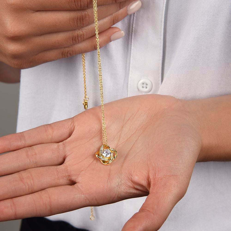 18k gold love knot necklace in a models hand