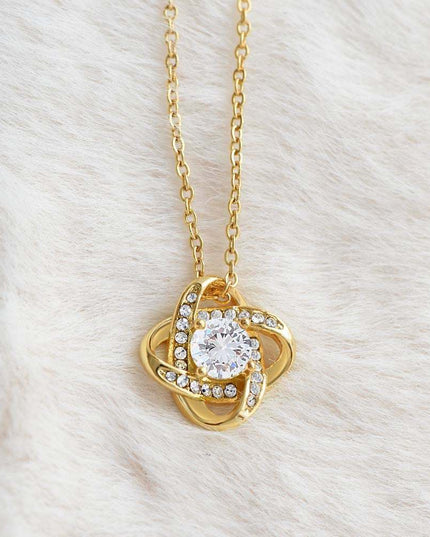 yellow gold love knot necklace on a white plush fabric up close