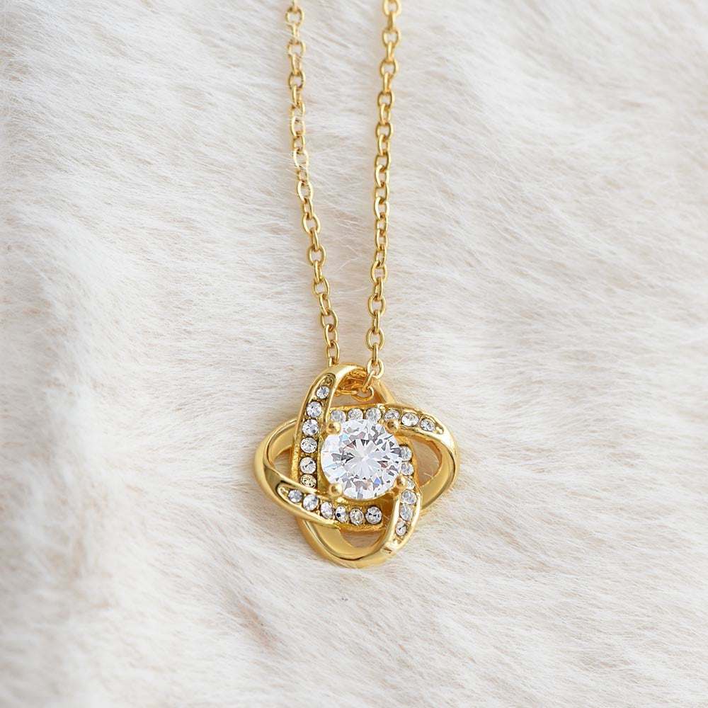 yellow gold love knot necklace on a white plush fabric up close