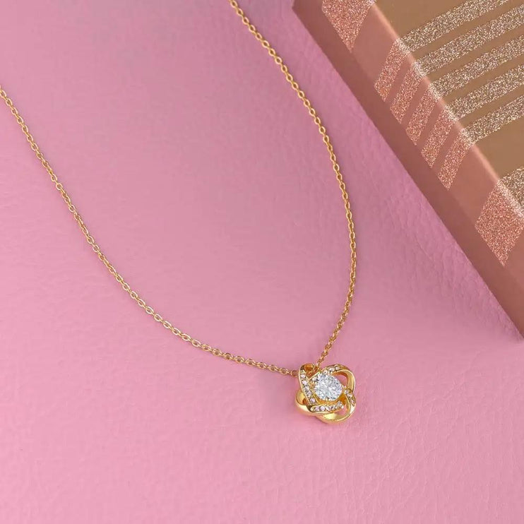 yellow gold love knot necklace laying on pink table