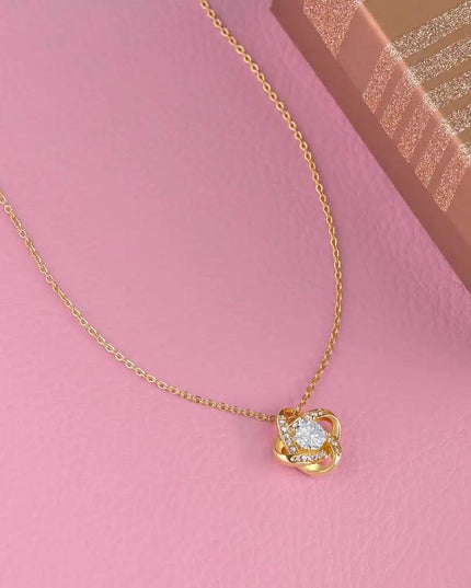 yellow gold love knot necklace on pink table