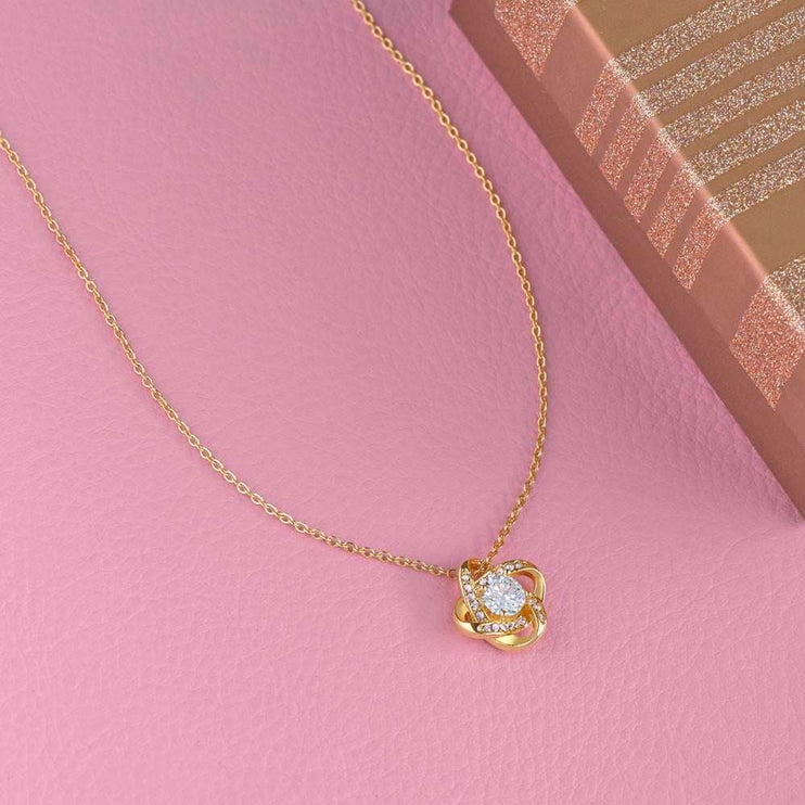 18k gold love knot necklace on a pink table