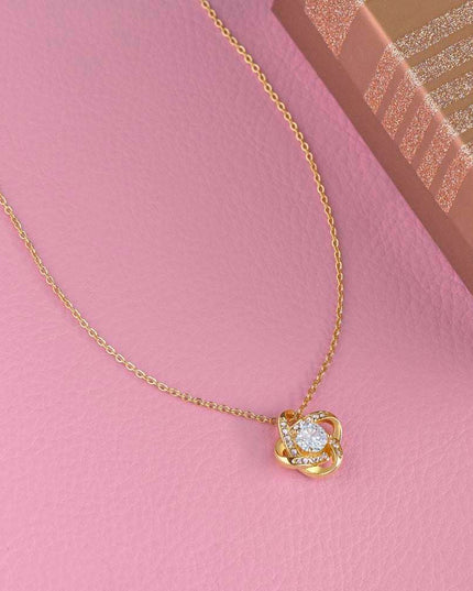 yellow gold love knot necklace on a pink display table
