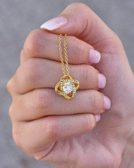 yellow gold love knot necklace in a model's hand