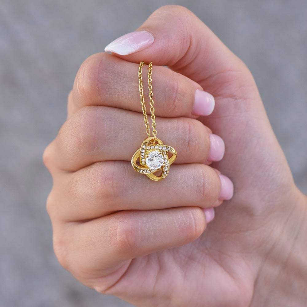 yellow gold love knot necklace in a model's hand