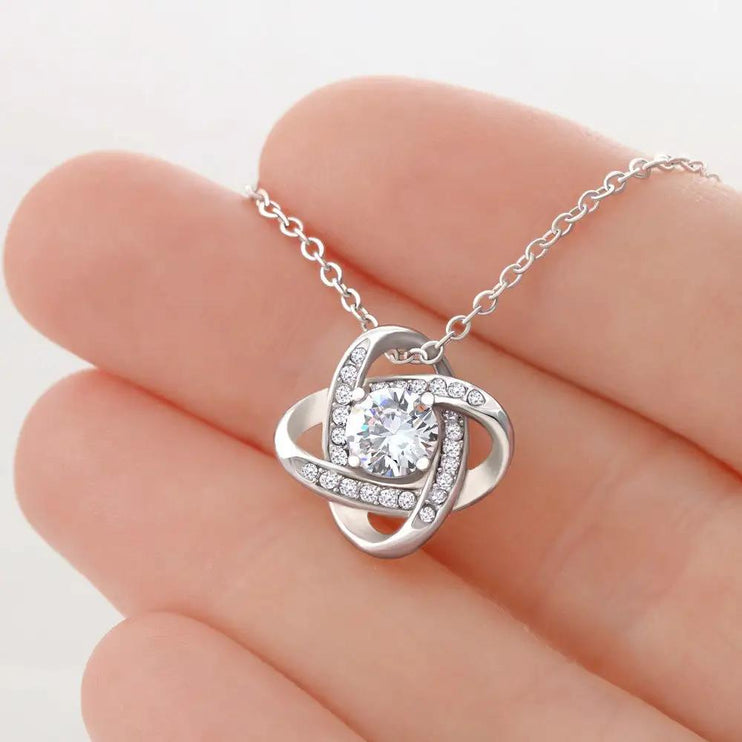 white gold love knot necklace in a model's hand