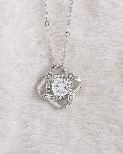 white gold love knot necklace on a white cloth showing charm up close
