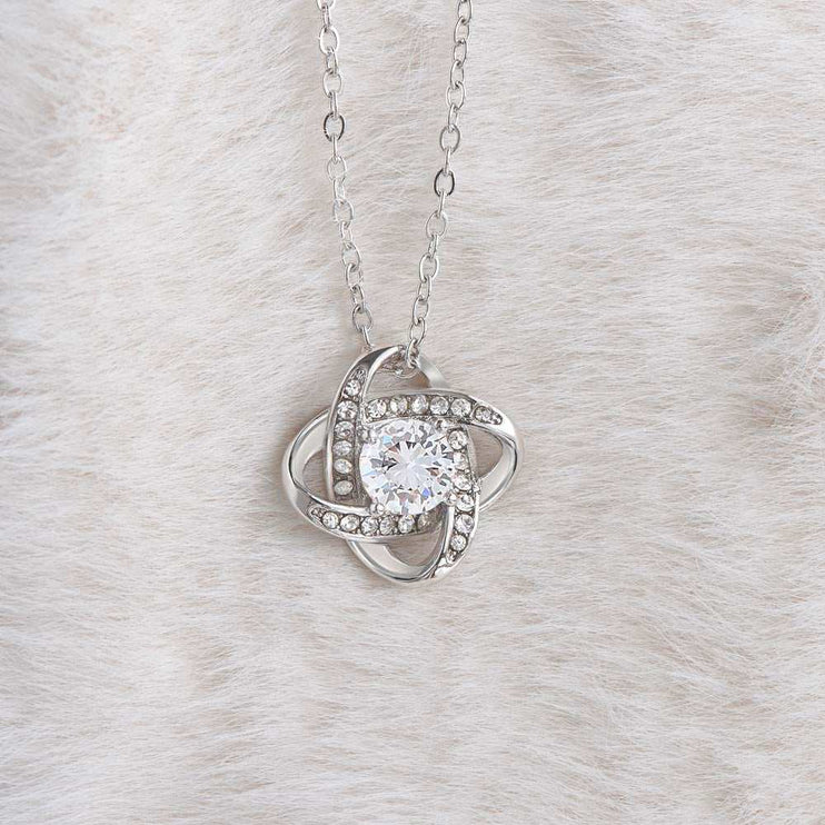 white gold love knot necklace on a white cloth showing charm up close