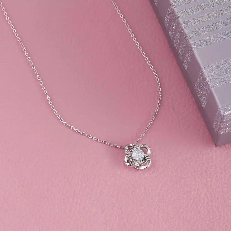 white gold love knot necklace on a pink table