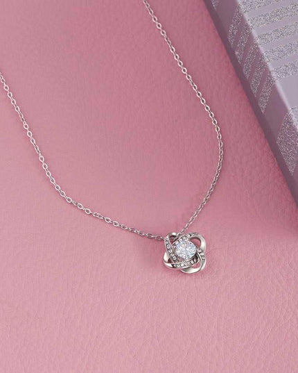 14k white gold love knot necklace on a pink table