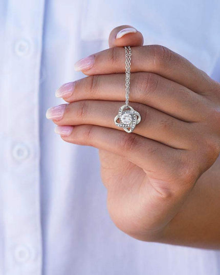 white gold love knot necklace up close of charm on a model's hand