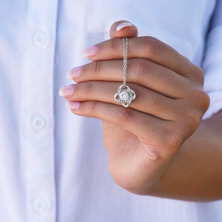 white gold love knot necklace up close of charm on a model's hand