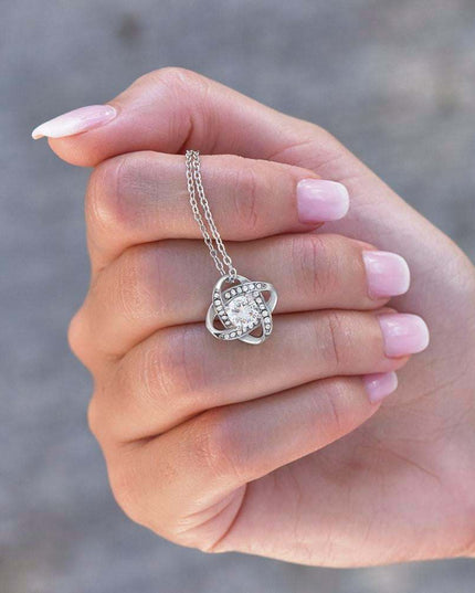 white gold love knot necklace in a model's hand